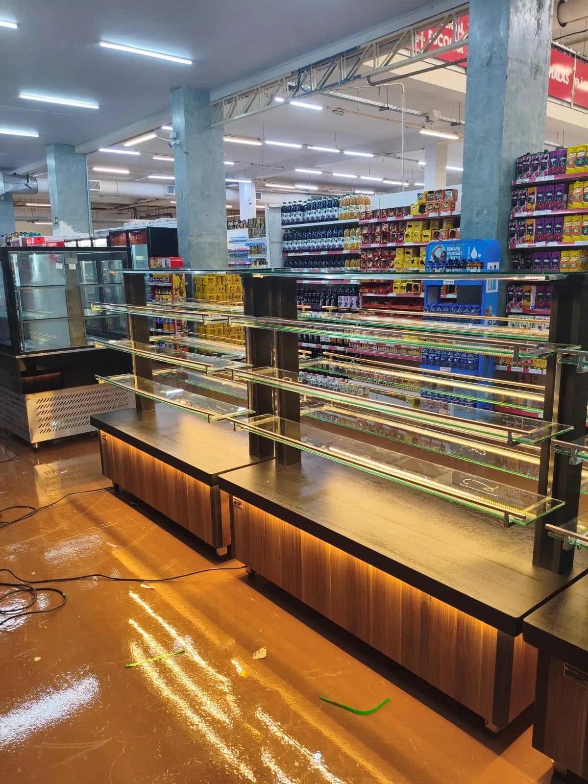Detalhes da ilha expositora com prateleiras de vidro, iluminação e acabamento amadeirado