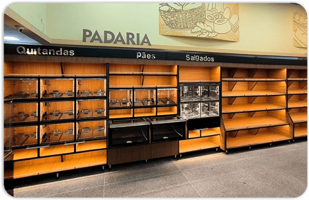 Área de padaria com expositores de pães, estrutura escura e acabamento amadeirado